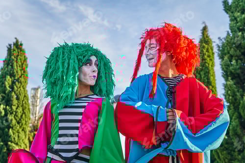 Preview: Happy clowns in multicolored costumes looking at each other in park