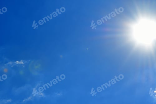 Preview: A vivid blue sky with the sun shining giving off sunbursts and sun flares with a few wispy clouds.
