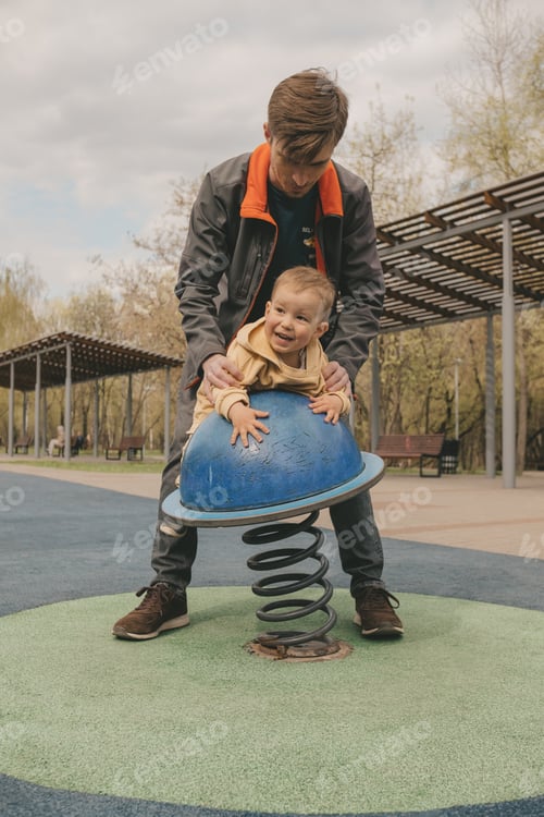 Preview: dad and child are walking on the playground.
dad spins a child on a carousel