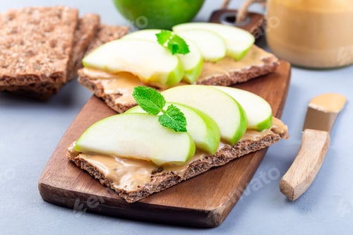 Preview: Sandwich with whole grain cracker, green apple slices and peanut butter, on wooden board, horizontal