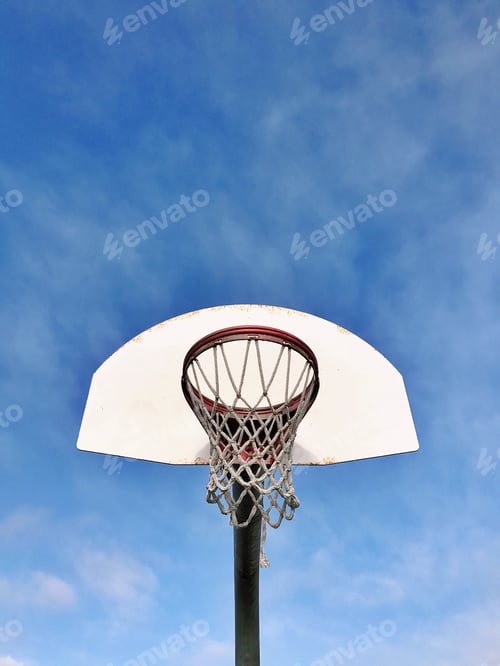 Preview: Looking up at an empty basketball hoop, net and backboard outdoors against a blue sky with clouds
