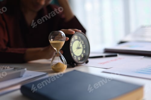 Preview: Man working at desk, holding clock with deadline document on table. Time management concept