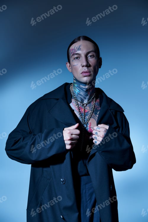 Preview: good looking stylish male model with tattoos posing with hands on his black coat, fashion concept