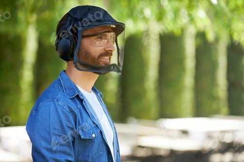 Preview: Smiling, bearded craftsmen in protective face shield and headset preparing for work outdoors.