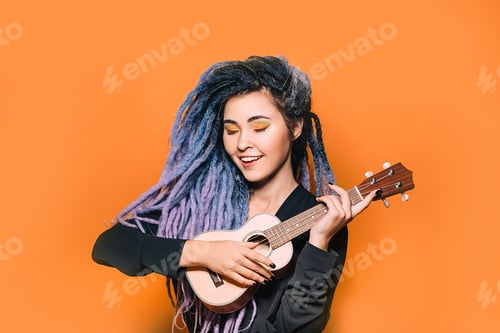 Preview: Rastafarian woman and dreadlocks and bright makeup plays on ukulele. Musical instrument ukulele