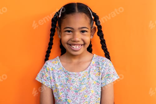 Preview: Portrait of happy biracial schoolgirl wearing t shirt over orange background at elementary school