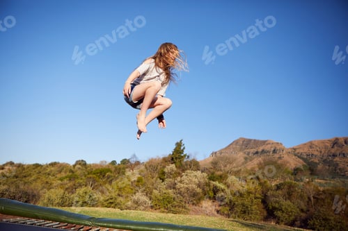 Preview: Young girl jumping on trampoline, mid air, in rural setting