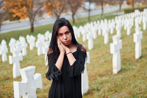 Preview: Young woman in black clothes visiting cemetery with many white crosses