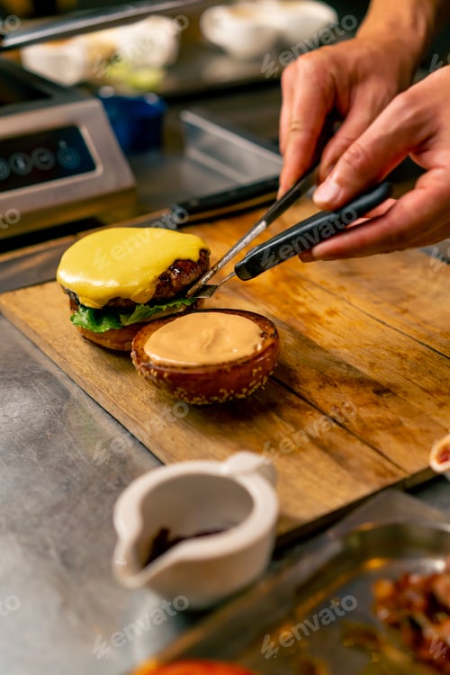 Preview: A close-up of a chef preparing a burger with beef patty with vegetables and cheese in the kitchen