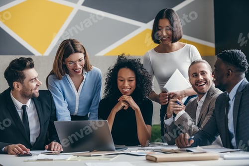 Preview: Smiling young business team looking at laptop while having group meeting in the office together