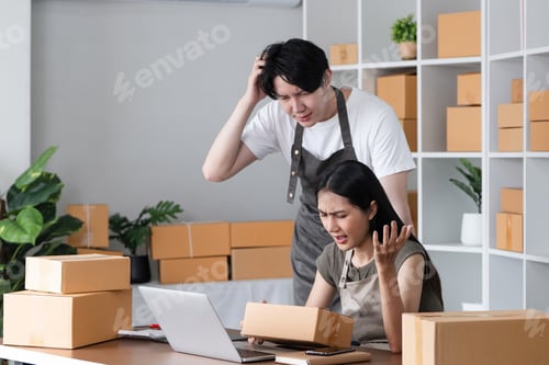 Preview: Stressed Couple Managing Online Sales Business at Home Surrounded by Cardboard Boxes and Laptop
