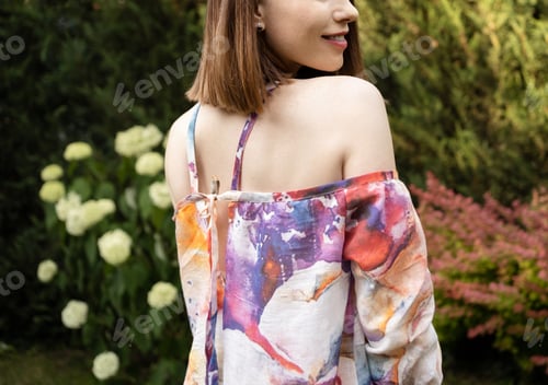 Preview: Summer moment. Cropped image of smiling Woman in colorful dress on green plants background, backyard