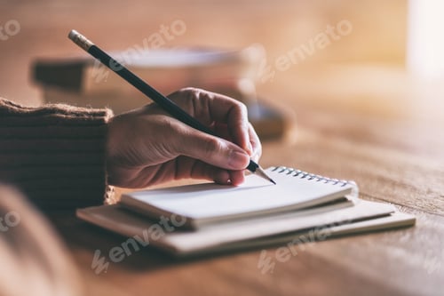 Preview: Closeup image of a woman writing on blank notebook on wooden table