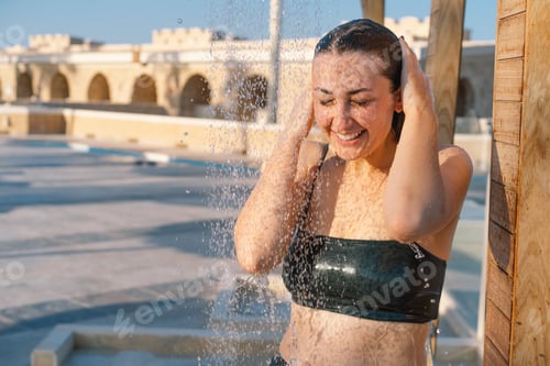 Preview: Beautiful young woman takes a relaxing shower in a swimsuit on a sunny day outdoors by the sea