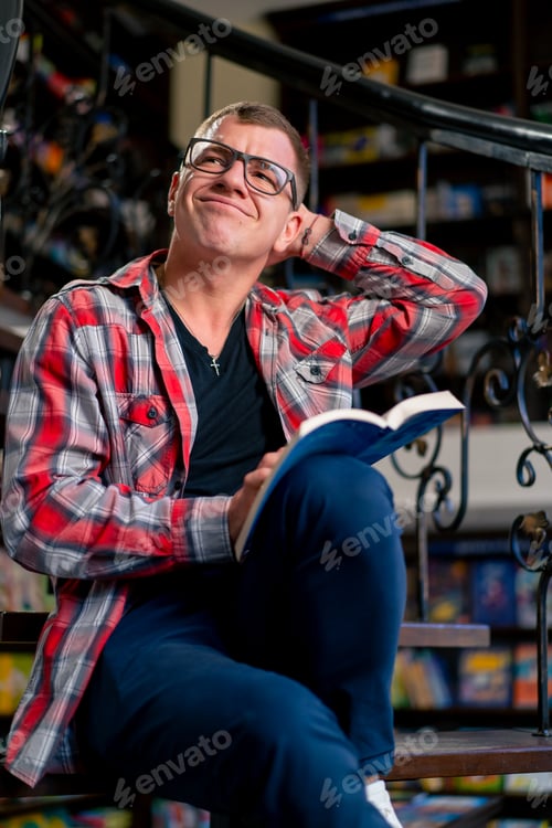 Preview: a man in glasses sits on the stairs in the library carefully reads a book and worries its characters