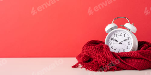 Preview: A vintage-style white alarm clock wrapped in a cozy red scarf against a vibrant red background