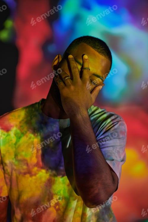 Preview: handsome man in street attire closing face with hand in digital projector lights, fashion concept