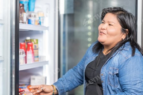 Preview: Smiling woman buying products of a fridge in a store