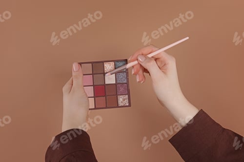 Preview: Woman with eyeshadow palette and brush on beige background, closeup