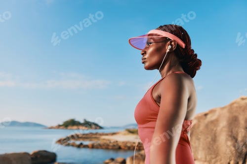 Preview: Woman in sportswear near the beach enjoying music with earphones and a visor