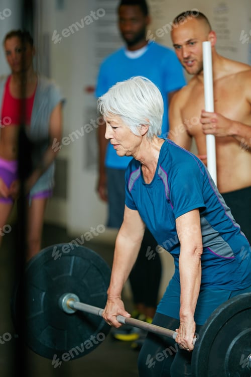 Preview: Shot of a senior woman lifting weights while a group of people in the background watch on