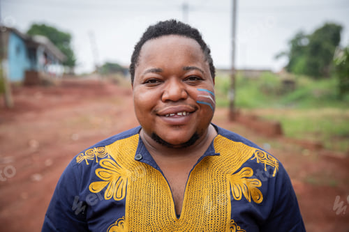 Preview: Outdoor portrait of smiling African trans person with trans flag drawn on cheek