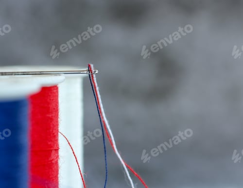 Preview: Closeup view of sewing thread in United States colors through the eye of the needle with copy space