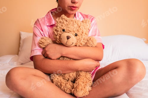 Preview: Unrecognizable young woman sitting on bed with teddy bear