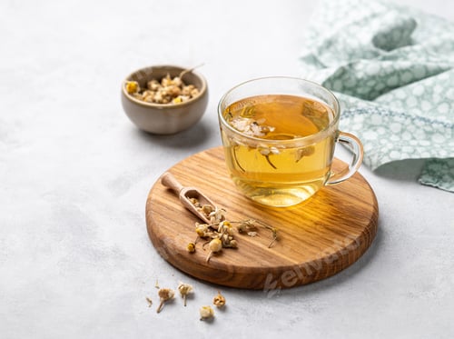 Preview: Chamomile herbal tea in a glass cup on a wooden board on a light background with dry flowers.