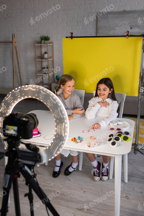 Preview: smiling preteen video bloggers talking near different accessories and digital camera in ring light