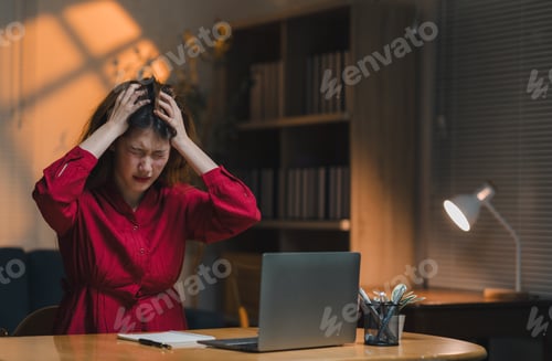 Preview: Stressed asian freelancer woman holding head in hands working at home office desk at night