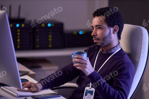 Preview: IT developer working at night writing code and drinking coffee at desk in office
