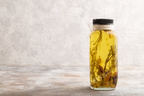 Preview: Sunflower oil in a glass jar with various herbs and spices onbrown concrete. Side view, copy space.
