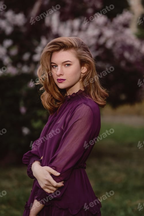 Preview: A beautiful young girl is standing in a purple dress in lilac flowers