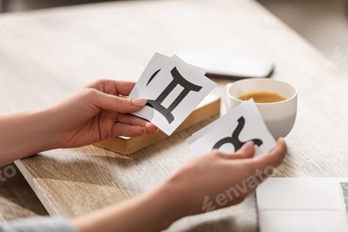 Preview: Cropped view of astrologer holding cards with zodiac signs beside coffee and book on table