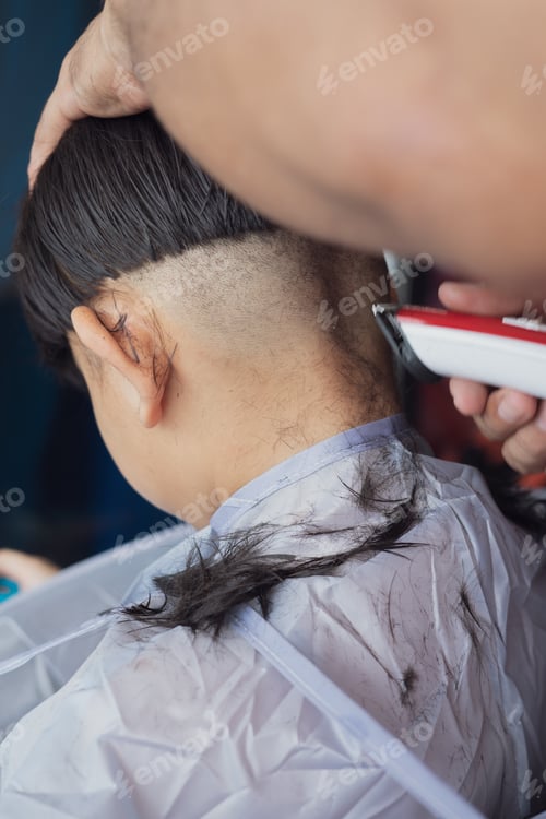 Preview: Asian child getting a haircut at home from the father. View from behind.
