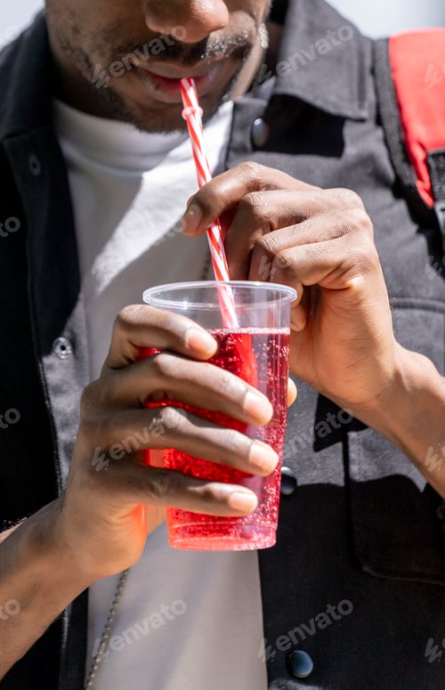 Preview: Close up view of a man with black skin drinking a soft drink through a straw