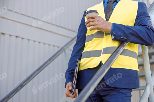 Preview: Male factory worker holding coffee to go and documents