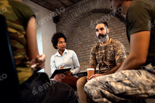 Preview: Female psychologist talking to group of diverse veterans during PTSD support group.