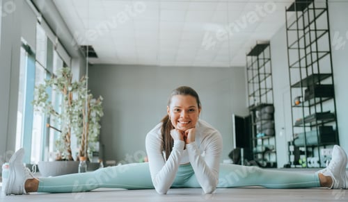 Preview: woman in a bright fitness outfit wears headphones and smiles while engaging in a stretch