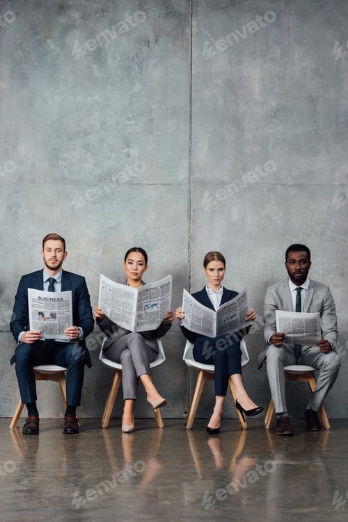Preview: serious multiethnic businesspeople sitting on chairs and reading newspapers in waiting hall