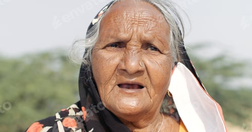 Preview: Closeup of an old South Asian woman with a Coronavirus face mask hanging down from her ear