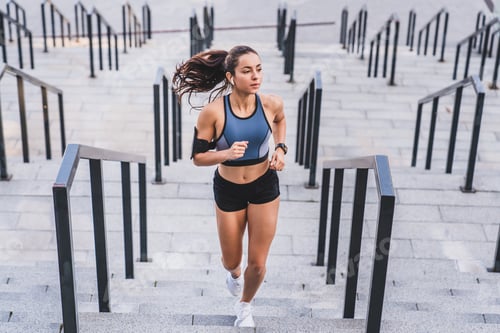 Preview: Full length photo of a young sporty female runner jogging on the stairs outdoors