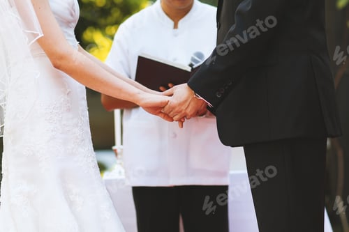 Preview: The midsection of the bride and groom hold hands at the wedding ceremony, close-up.