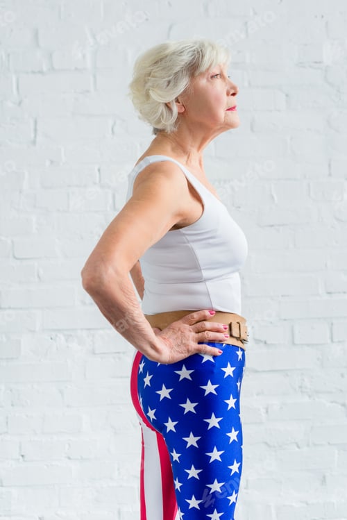 Preview: side view of senior woman in sportswear standing with hands on waist and looking away