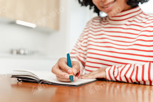 Preview: Portrait of smiling positive African American woman holding pen, taking notes in notebook