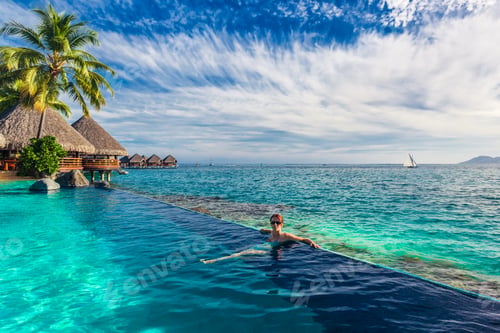 Preview: Woman in the infinity pool in exotic island resort with bunalows