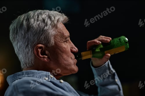 Preview: Senior Man Drinking From Green Beer Bottle Indoors