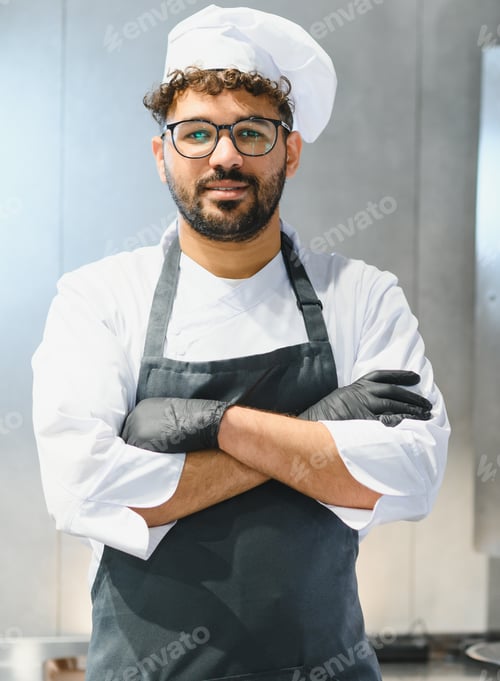 Preview: Confident middle eastern chef wearing black gloves posing in kitchen