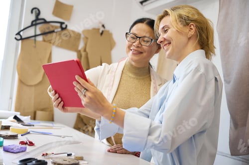 Preview: Smiling ladies fashion designers using tablet at workplace